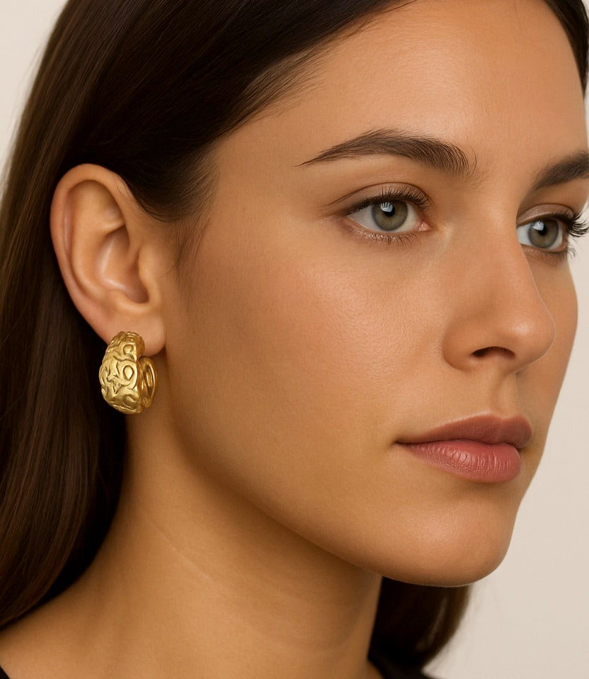 Close-up of a woman wearing gold hoop earrings with a neutral background