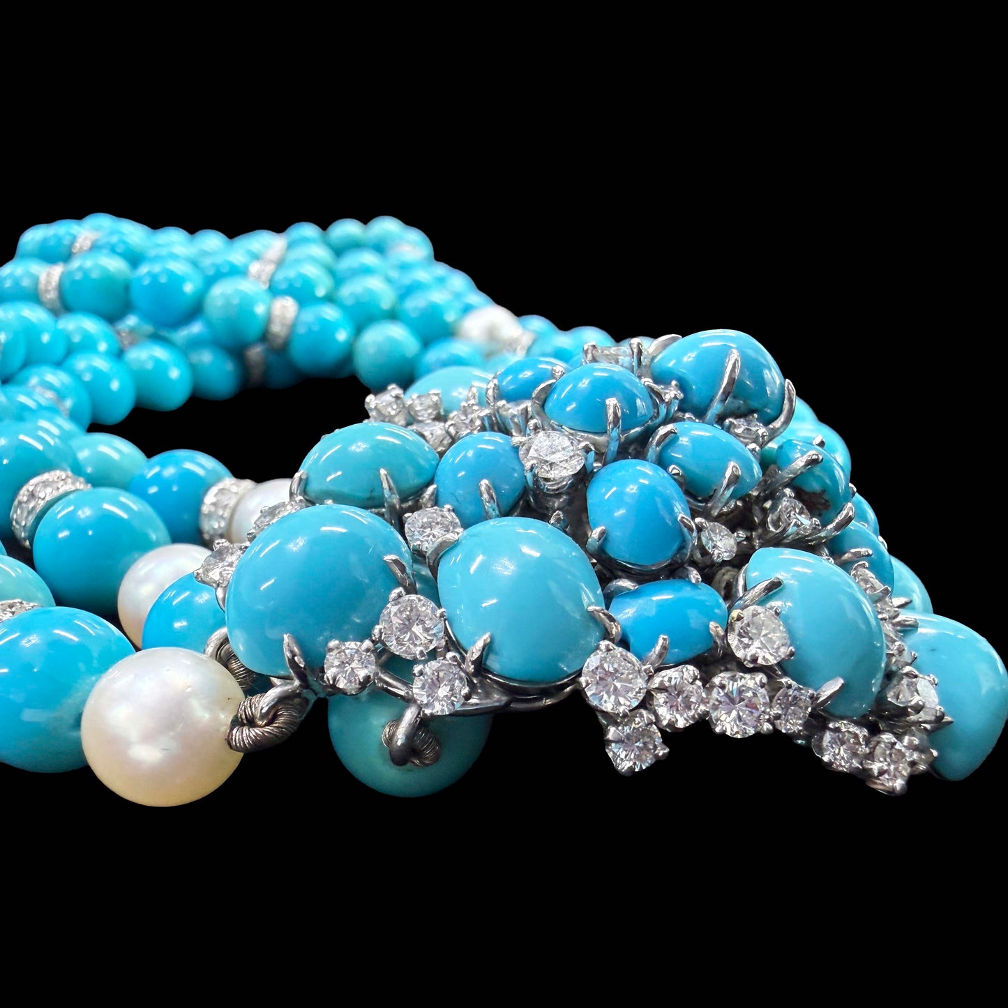 Signed Meister. A close-up of a multi-strand turquoise necklace with silver-toned metal settings and clear gemstones, alongside a single white pearl, photographed against a solid black background.