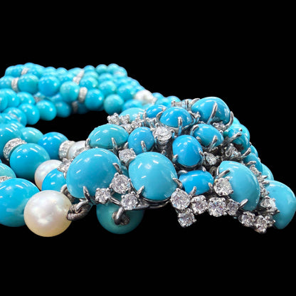 Signed Meister. A close-up of a multi-strand turquoise necklace with silver-toned metal settings and clear gemstones, alongside a single white pearl, photographed against a solid black background.