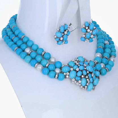 meister-swiss-18k-turquoise-diamond-pearl-necklace-earring-suite A turquoise blue beaded statement necklace with matching stud earrings displayed on a white mannequin bust. The necklace features multiple strands of round turquoise beads, silver spacer rings, and faux pearl accents, with a large central floral cluster embellished with turquoise, silver, and clear rhinestones.
